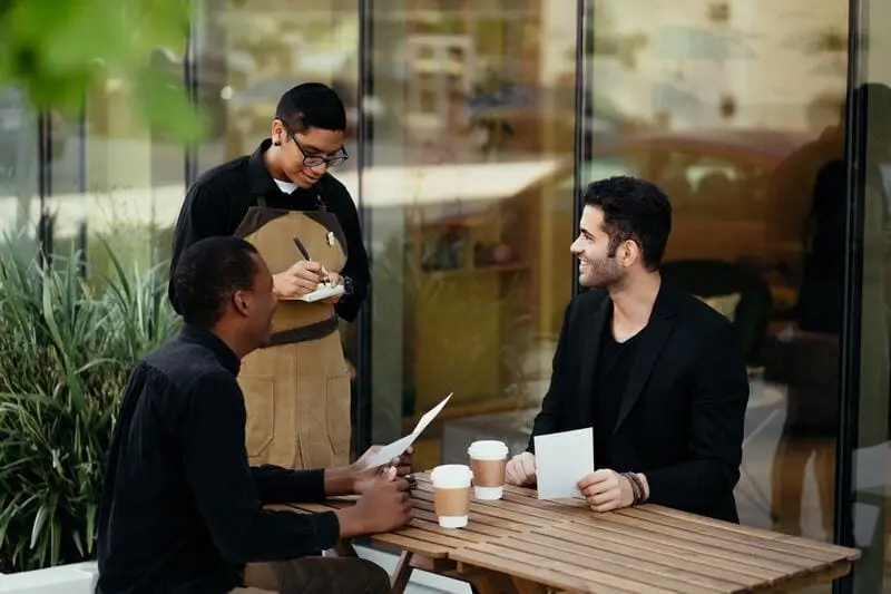 clients assis en terrasse souriant buvant du café serveur prenant commande