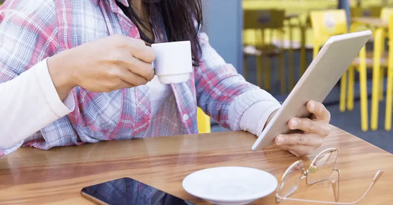 femme chemise à carreaux tenant une tablette tactile et un café