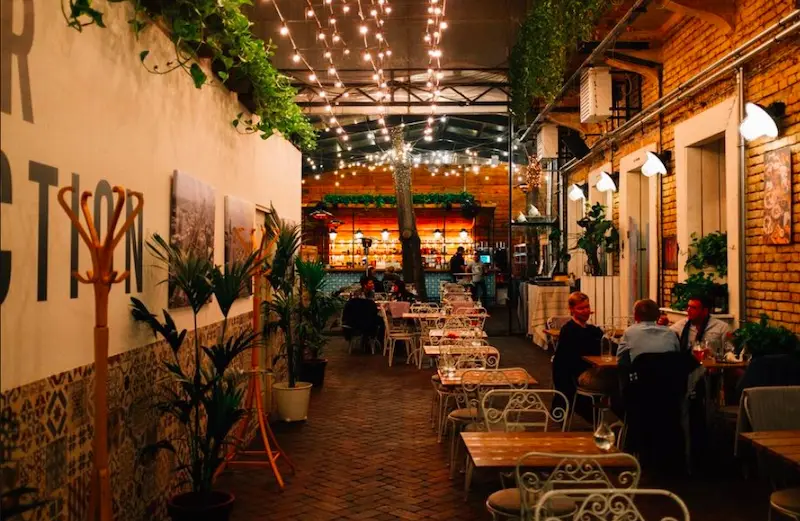 salle tamisée tables en bois chaises blanches en fer guirlandes lumineuses porte manteaux plantes vertes